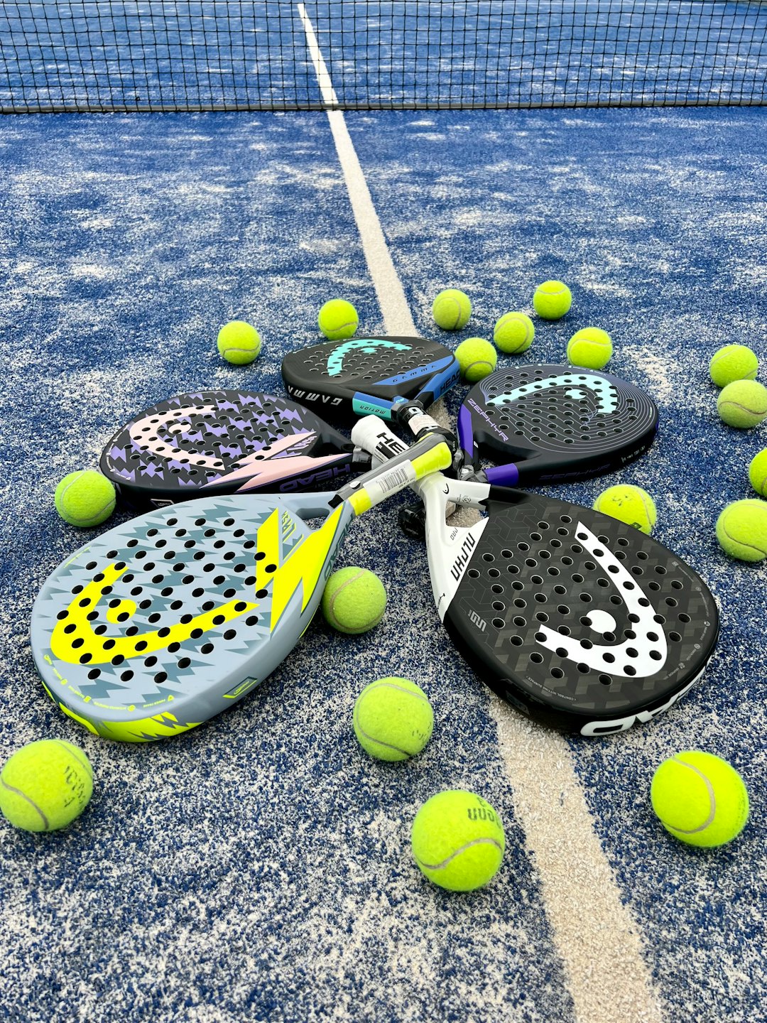 Raquetas y pelotas de pádel de colores en una cancha azul.