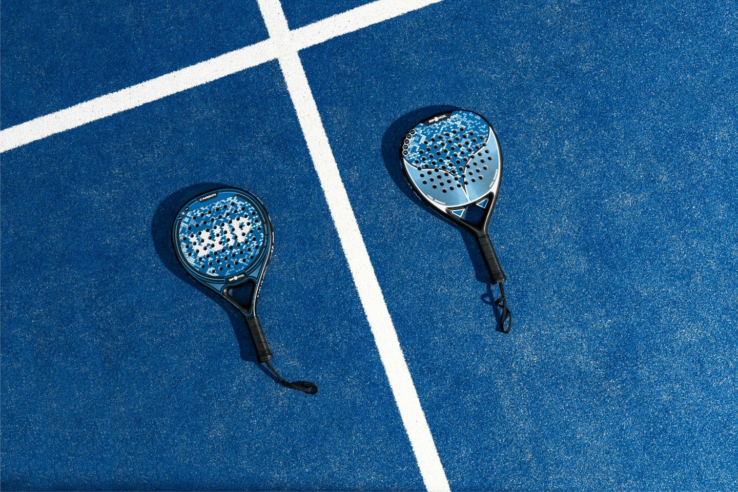 Dos palas de pádel apoyadas en una pista azul con líneas blancas.